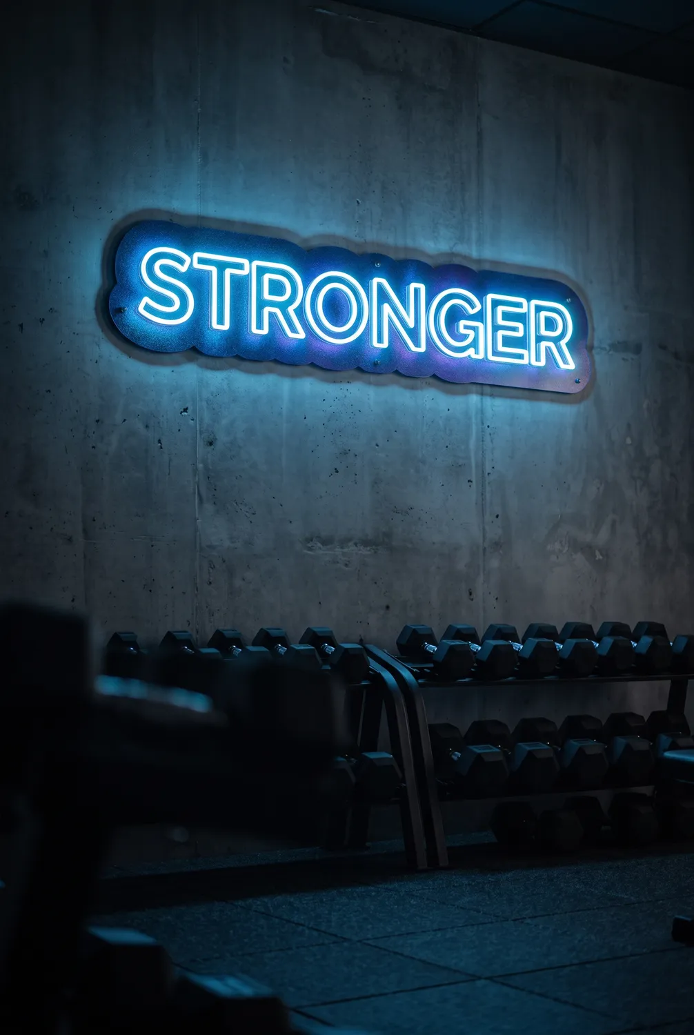 Ice blue &lsquo;STRONGER&rsquo; neon sign on an iridescent blue cosmos backboard in a modern private gym