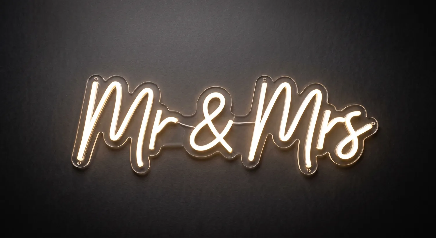 Warm white &lsquo;Mr & Mrs&rsquo; neon sign on clear laser-cut acrylic against a dark textured wall